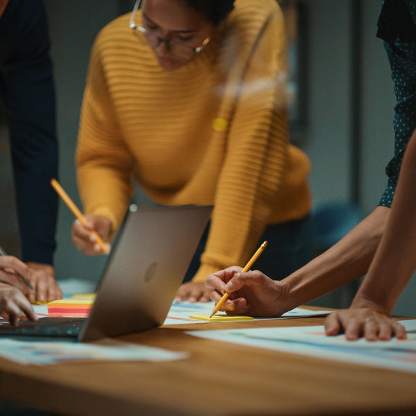 Close-up of colleagues gathered around a table, writing on sticky notes and reviewing documents together during a collaborative planning session.