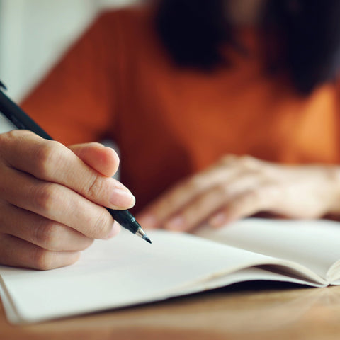 Person writing notes in a notebook during a formal review or discussion process, representing careful documentation and structured questioning techniques.