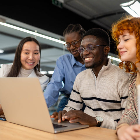 Group of four people working together on a laptop in an office setting.