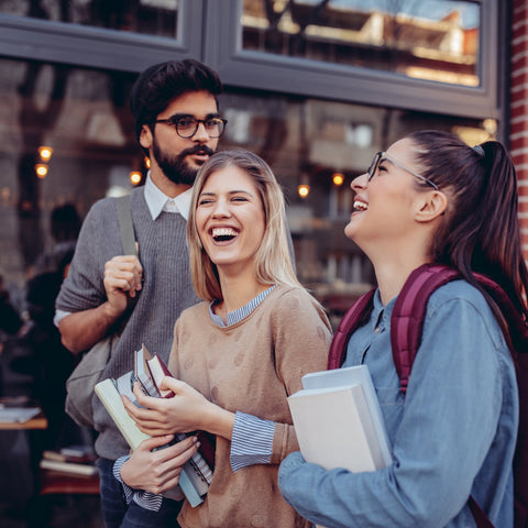 Three friends laughing together outside a building with a brick wall.