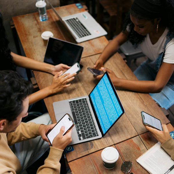 Four college students studying together at a table with laptops, phones, and notes.