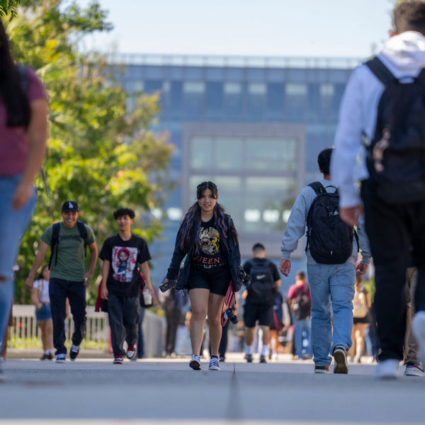 Students walking on a campus path with trees and buildings in the background