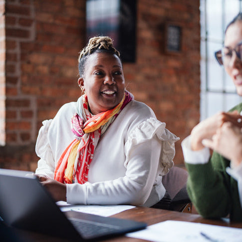 Two coworkers engaged in a professional conversation at a desk, discussing work collaboratively and representing effective communication and conflict resolution.
