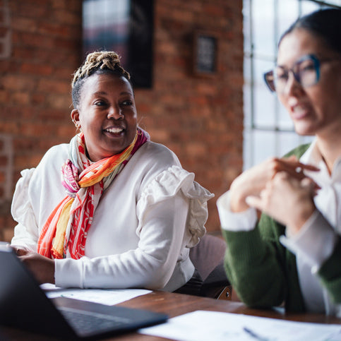 Two coworkers engaged in a professional conversation at a desk, discussing work collaboratively and representing effective communication and conflict resolution.