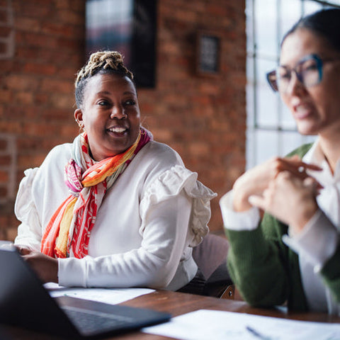 Two coworkers engaged in a professional conversation at a desk, discussing work collaboratively and representing effective communication and conflict resolution.