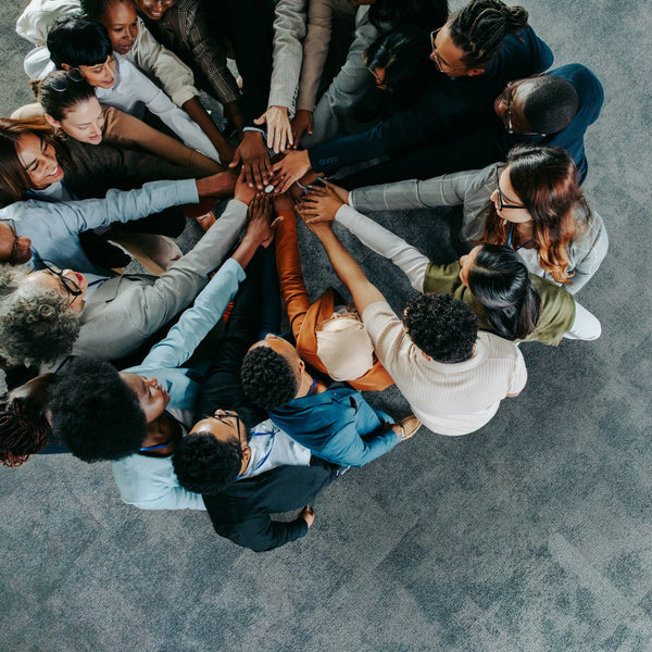 Diverse group of people standing in a circle with hands stacked together, symbolizing teamwork, unity, and collaboration.