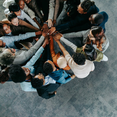 Diverse group of people standing in a circle with hands stacked together, symbolizing teamwork, unity, and collaboration.