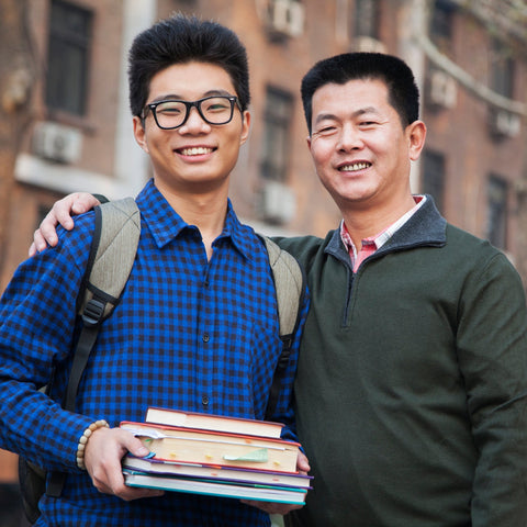 Two men standing outdoors with one holding books, in front of a brick building.