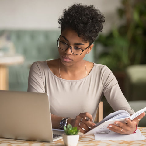 Woman working on a laptop with notes at a table in a home office setting