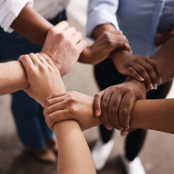 Four people of diverse skin tones clasp wrists together in a close-up circle.