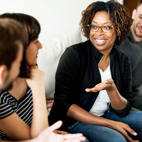 Group of people sitting together, with a woman in glasses speaking.