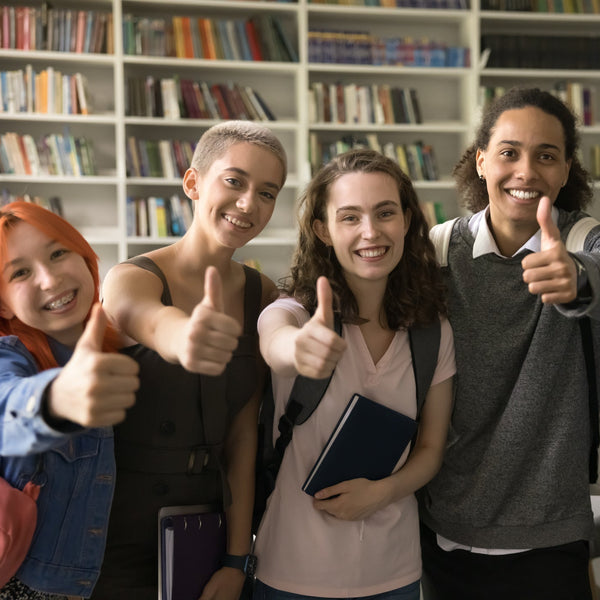 Four students giving thumbs up in a library setting