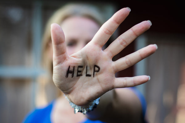 Close-up of a woman's hand with "HELP" written on her palm, held toward the camera.

