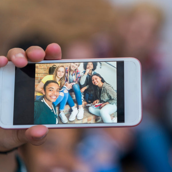 Smartphone displaying a group photo of smiling college students, representing authentic student storytelling and campus engagement for orientation, marketing, and recruitment.