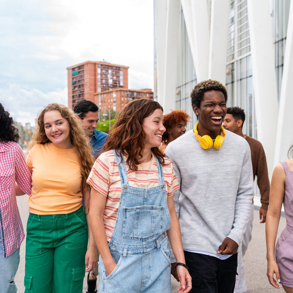 Diverse group of college-aged students walking together outdoors, smiling and talking, showing friendship and connection on a modern campus.
