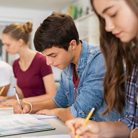 Students sitting at a table with notebooks and pens in a classroom setting.