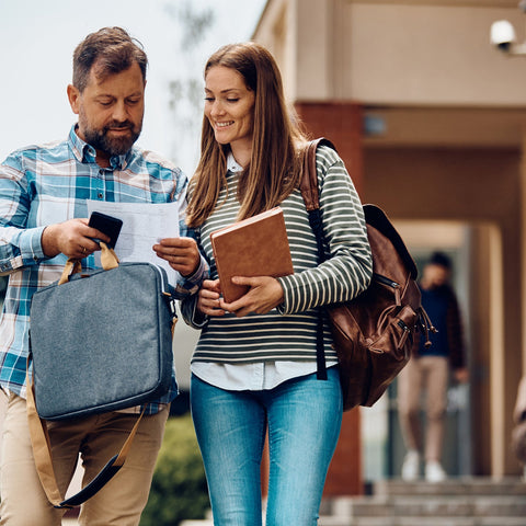 Man and woman walking outside a building, holding bags and books