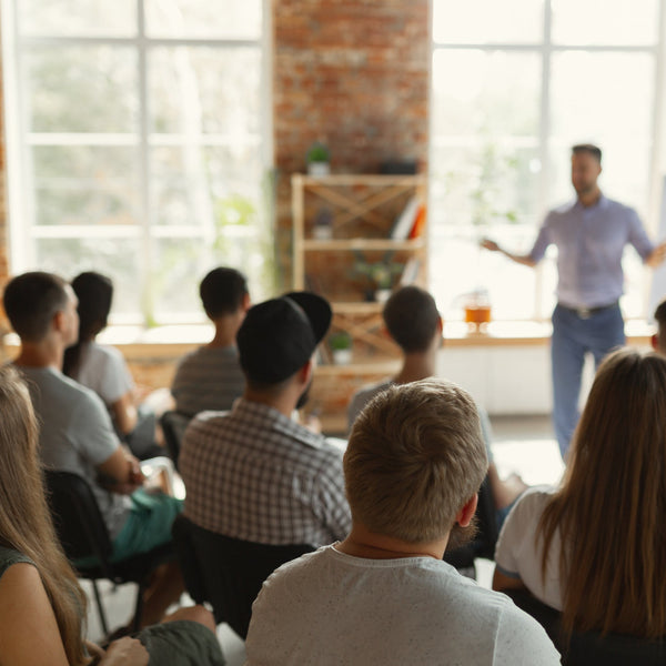 Male speaker presenting to a seated audience in a university workshop hall.