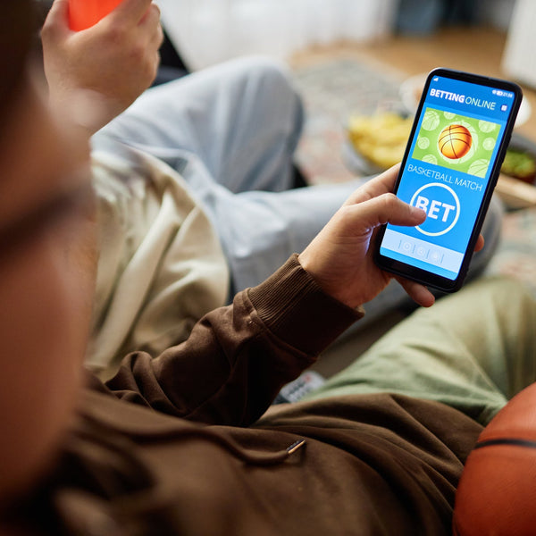 Young man on a couch placing a sports bet on a basketball match through a mobile betting app