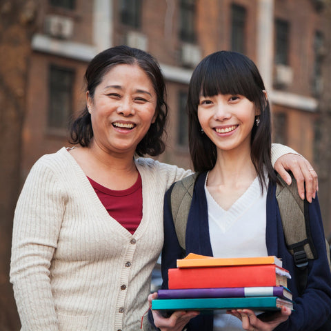 Two women standing together, one holding books, in an urban setting.