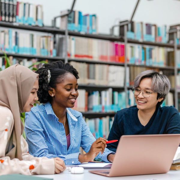 Three students studying together in a library with a laptop.