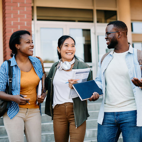 Three students standing on a school staircase, smiling and engaged in conversation.