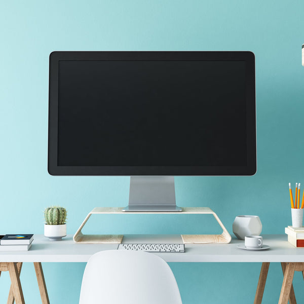 Modern office desk with computer monitor, office supplies, and a light blue wall.