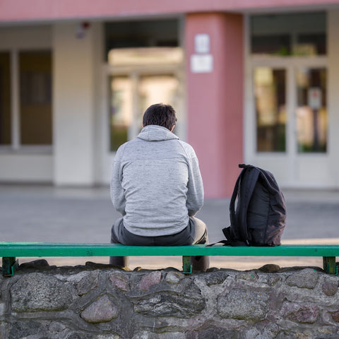 Person sitting on a bench in front of a building with a backpack