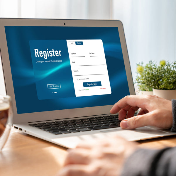 Person using a laptop to complete an online registration form, with a coffee and desk supplies nearby, representing a clean and user-friendly digital signup experience.
