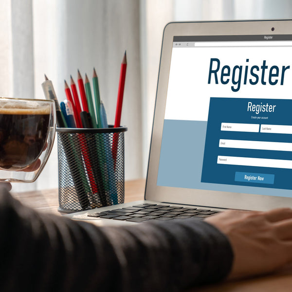 Person using a laptop to complete an online registration form, with a coffee and desk supplies nearby, representing a clean and user-friendly digital signup experience.