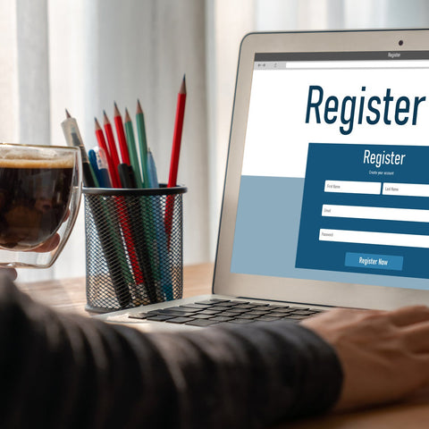 Person using a laptop to complete an online registration form, with a coffee and desk supplies nearby, representing a clean and user-friendly digital signup experience.