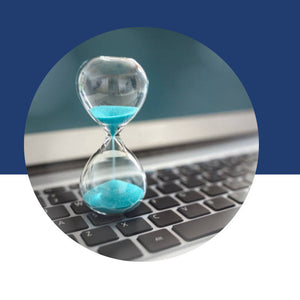 An hourglass with blue sand draining, sitting on top of a laptop keyboard.