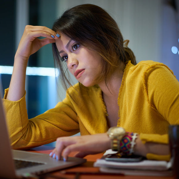 Woman in yellow sweater sitting at a desk with a laptop, looking tired.