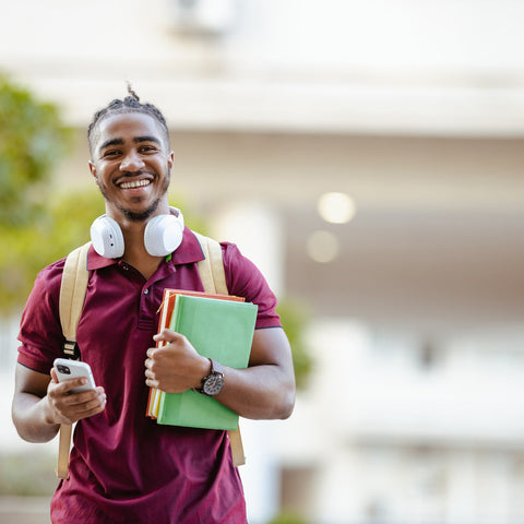 Man holding books and a phone, smiling outdoors