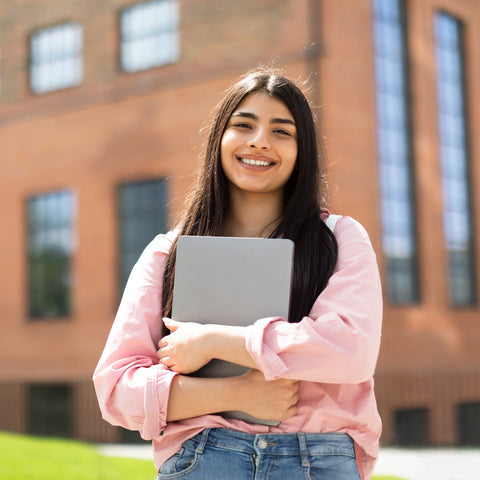 Young woman holding a laptop outdoors in front of a brick building
