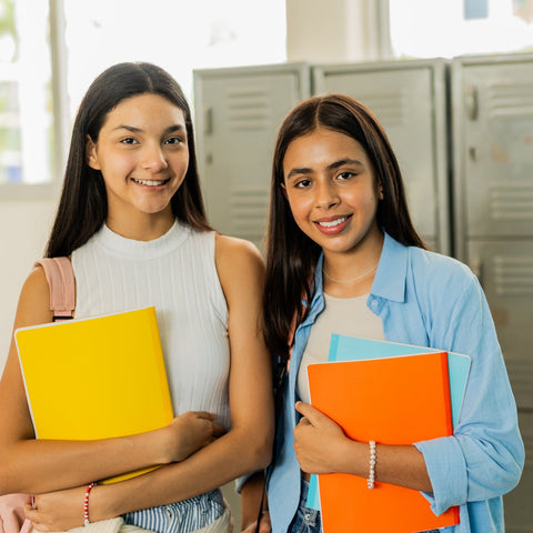 Two students standing in front of lockers holding colorful books.