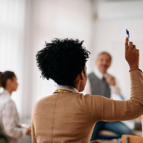 Professional raising their hand during a workplace training or discussion, representing confidence, participation, and self-advocacy skills.