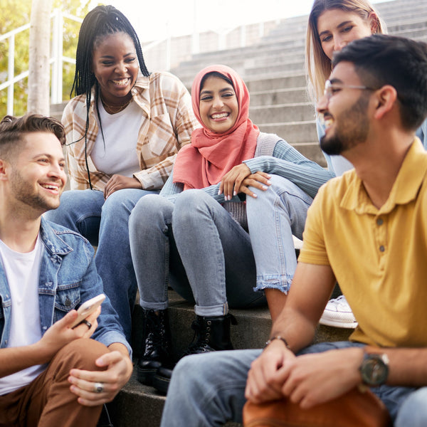 Group of young adults sitting on steps outdoors, smiling and interacting.