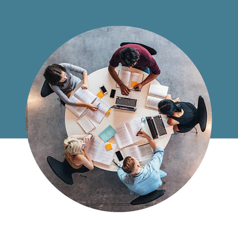 Top-down view of people working around a table with laptops on a blue background
