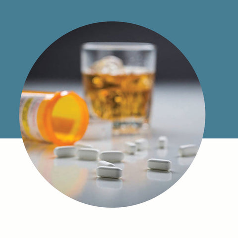 Spilled prescription pill bottle next to a glass of alcohol on a blue and white background.