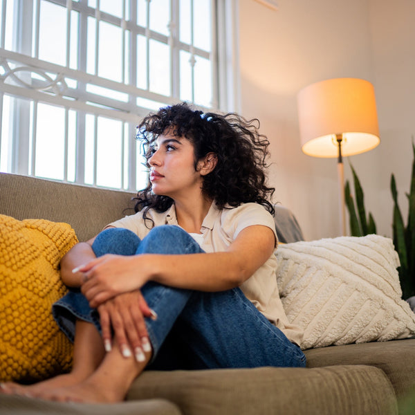 Woman sitting on a couch in a living room with a lamp and plants in the background