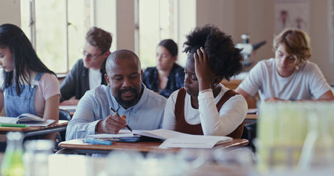 Teacher assisting a student with coursework in a classroom.