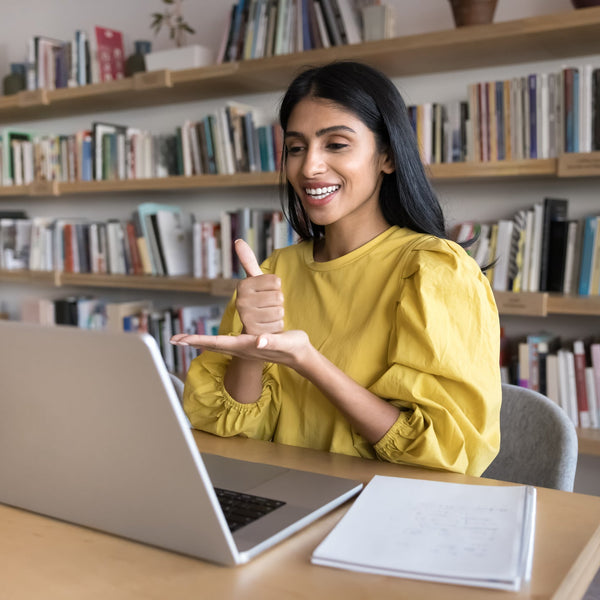Woman in yellow shirt using laptop in a library setting