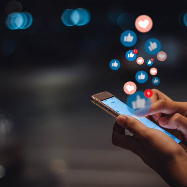 Person using a smartphone with social media icons above, blurred lights in the background
