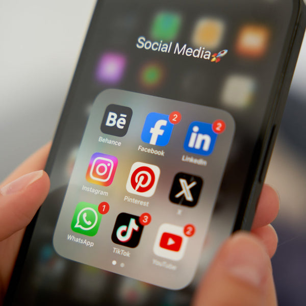 Hand holding a smartphone with social media app icons displayed on the screen.