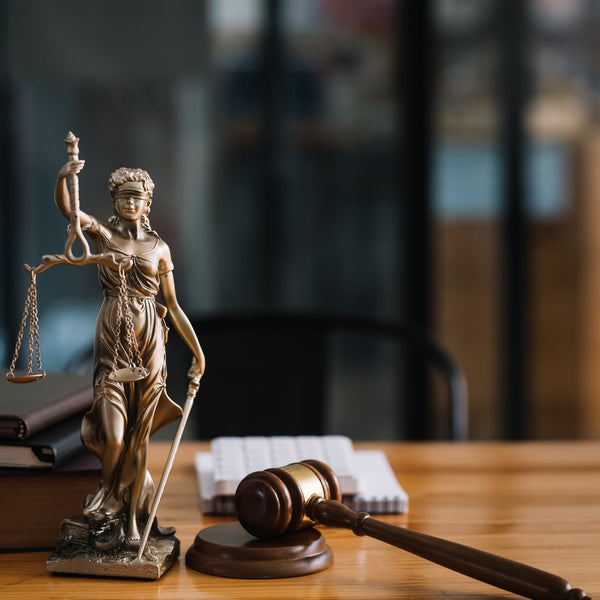Statue of Lady Justice with a gavel on a wooden desk in an office setting