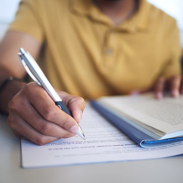 Person writing in a notebook with a pen on a table.