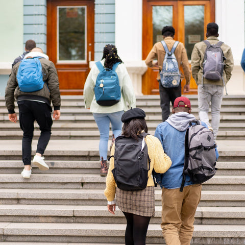 Group of students with backpacks walking up a set of stairs in front of a school building.