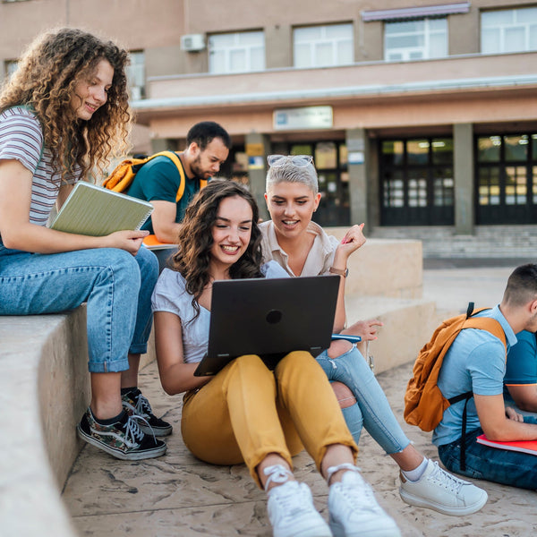 Group of students sitting outdoors with a laptop and books