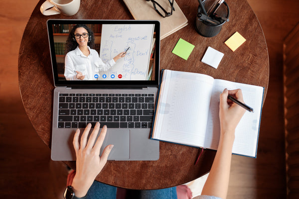 Person attending a virtual meeting on a laptop with notes and a coffee cup on a wooden table.